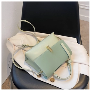 Détail du sac à bandoulière vert clair avec boucles dorées sur une veste blanche
