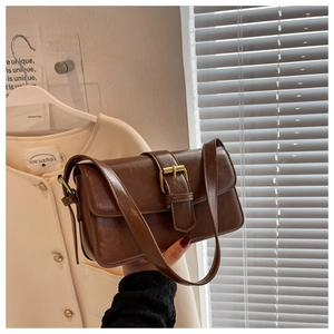 Detail of dark brown leather shoulder bag with glossy oil wax texture and gold metal buckle