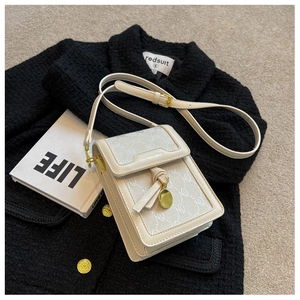 Close-up of cream crossbody bag with leather tassels and gold coin charm on tweed