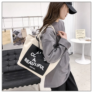 Detail of a large cream canvas tote bag featuring black artistic text and side leather tag