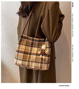 Detail of tartan canvas tote bag with brown leather strap and plush monster charm
