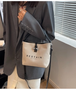Detail of canvas bucket bag with black leather trim, T-bar clasp and adjustable strap