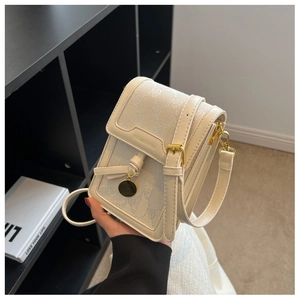 Close-up of a cream square crossbody bag featuring monogram fabric and adjustable strap
