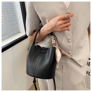 Détail du sac seau noir en cuir grainé avec élégant foulard en soie enroulé sur la poignée