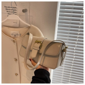Detailed shot of beige faux leather shoulder bag featuring vintage gold buckle and long strap