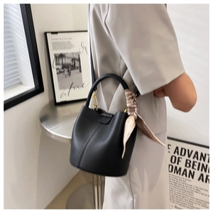Détail du sac seau noir en cuir grainé avec un foulard en soie décoratif sur la poignée