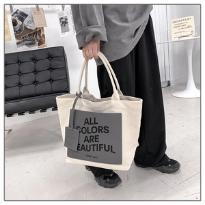 Detail of minimalist canvas tote bag with contrast patch and slogan held by a model