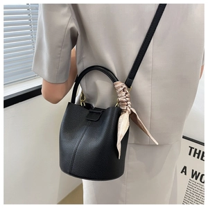 Détail du sac seau noir en cuir grainé avec foulard en soie porté en bandoulière