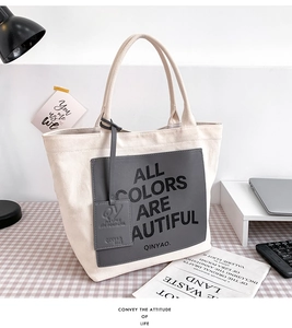 Detail of canvas tote bag with gray leather patch and slogan on plaid tablecloth