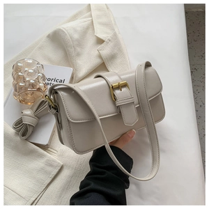 Detail of creamy white crossbody bag with gold metal buckle on elegant blazer backdrop