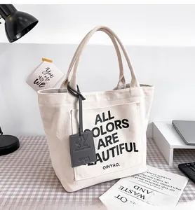 Detail of cream canvas tote bag featuring ALL COLORS ARE BEAUTIFUL slogan and branding