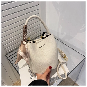 Détail du sac seau crème en cuir grainé avec foulard en soie enroulé sur la poignée