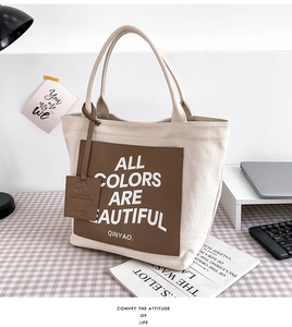 Close-up of cream canvas tote with brown leather patch and slogan on a desk background