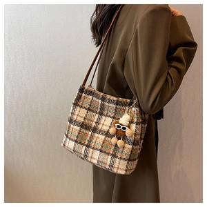 Detail of a brown plaid tweed tote bag with plush doll pendant and leather straps
