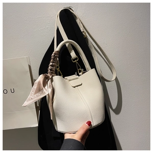 Gros plan sur un sac seau beige grainé avec foulard en soie et bandoulière en cuir