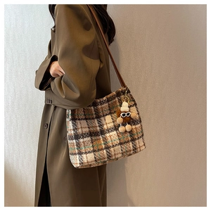 Detail of vintage plaid canvas tote bag with brown leather strap and plush doll charm