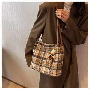 Detail of tweed checkered tote bag with plush bear charm and brown leather shoulder strap
