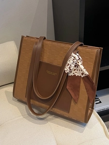 Brown leather tote bag with grid texture and decorative scarf in a lifestyle setting