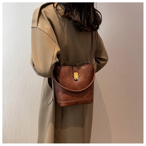 Detailed view of a vintage brown bucket bag with gold metallic twist lock on camel coat