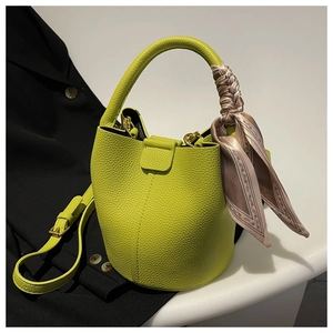 Détail du sac seau vert vif en cuir texturé avec un foulard en soie imprimé décoratif