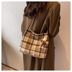 Detail of vintage plaid canvas tote bag with brown leather straps and plush bear charm