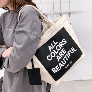 Minimalist beige canvas tote bag with black slogan patch and shoulder strap for women