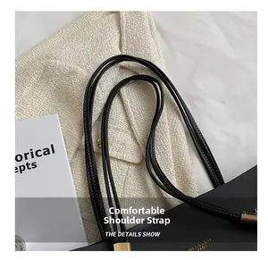 Detail of black leather tote bag showing white stitching on straps and gold logo