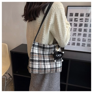 Detail of checkered canvas tote bag with black leather strap and plush monster charm