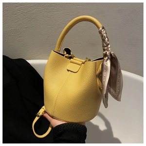 Détail du sac seau en cuir jaune avec un foulard en soie autour de la poignée