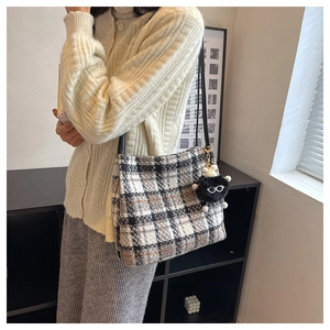 Detail of checkered tweed tote bag with plush monster charm and leather shoulder strap