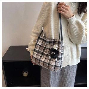 Close-up of wool plaid tote bag with black leather straps and furry monster charm