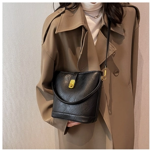 Classic black leather bucket bag with gold clasp shown on a trench coat model