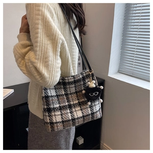 Detail of grey plaid tweed tote bag with black strap and cute monster plush charm