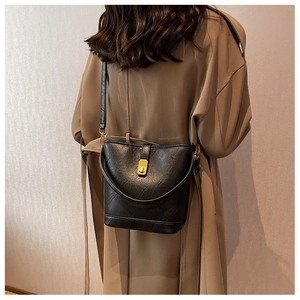 Detail of minimalist black leather bucket bag with gold clasp on khaki trench coat