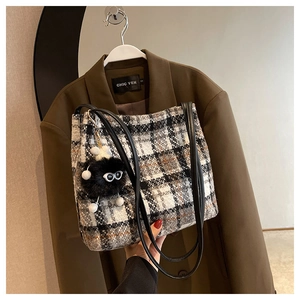 Close-up of a plaid tote bag featuring a black fuzzy monster charm on a brown blazer background