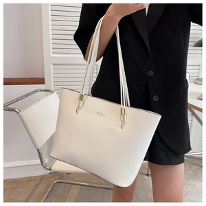 Close-up of minimalist white leather tote bag with gold rings and black suit contrast