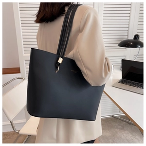 Detail of minimalist black tote bag with gold buckle straps in office setting