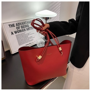 Detail of red matte leather tote bag with gold hardware and logo, held by a model