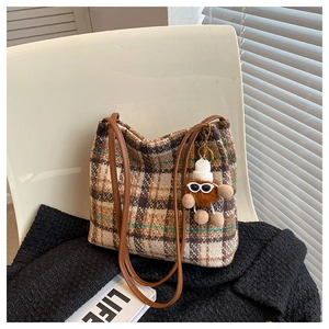 Detail of tweed checkered tote bag with brown leather handles and plush doll pendant