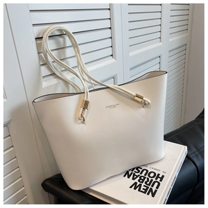Detailed close-up of white leather tote bag with gold logo and premium metal hardware