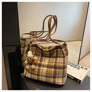 Detail of checkered canvas tote bag with brown leather handles and plush charm accessory