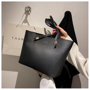 Close-up of black matte leather tote bag featuring gold logo and long shoulder handles