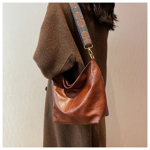 Brown leather hobo bag with a retro patterned wide strap shown on a winter coat