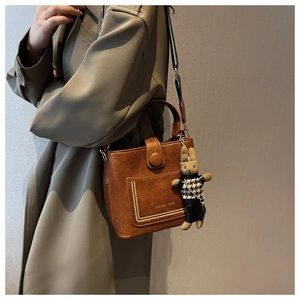Detail of brown leather bucket bag with Monday. Vera logo and cute rabbit charm pendant