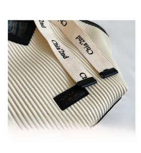 Detailed view of cream pleated tote bag featuring woven straps with black logo branding