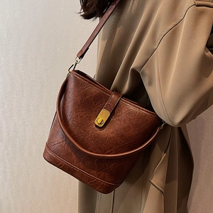 Deep brown vintage oil wax leather bucket bag with gold clasp shown on woman in trench coat