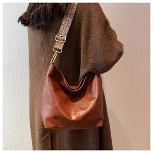 Brown leather hobo bag with ethnic style wide strap shown on model over wool coat