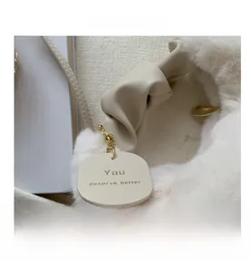 Detail of white faux fur texture and beige knotted handle with gold chain tag