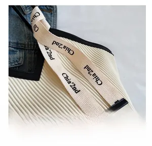 Detail of white pleated tote bag featuring beige webbing strap and black leather trim