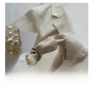 Detail of plush off-white handbag featuring a ruched handle and elegant gold chain strap